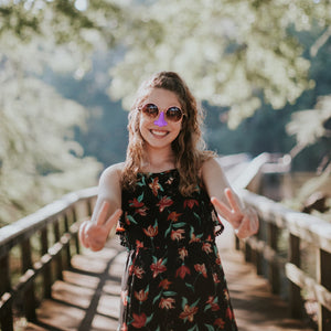 smiling woman wearing sunglasses and reef safe purple waterproof spf sunscreen on nose